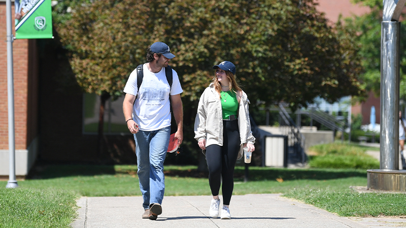 Two young adults walking on a university campus pathway looking at eachother.
