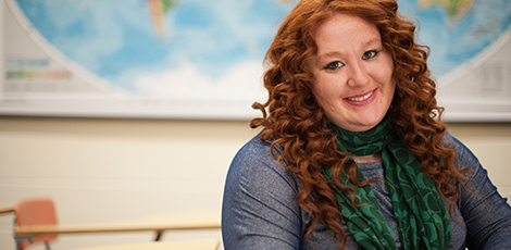 A woman smiling at the camera with a world map behind her