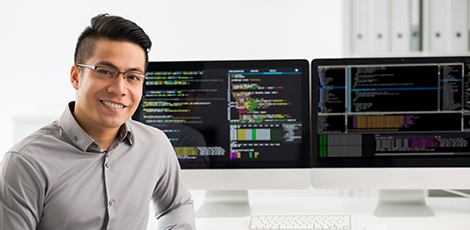 A man smiling in front of a computer displaying code