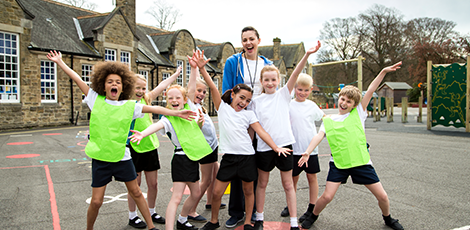 A group of kids and their teacher standing in the street throwing up their arms in glee