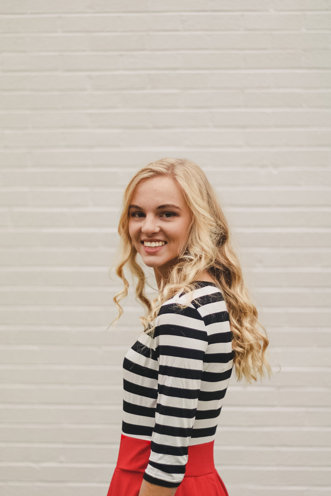 Annah stands in front of white wall in red skirt and striped shirt.jpeg