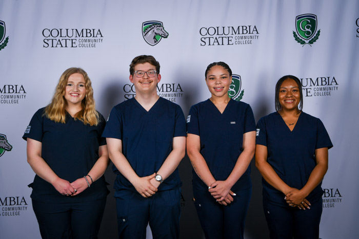 Four people pose for a photo in front of a white background.