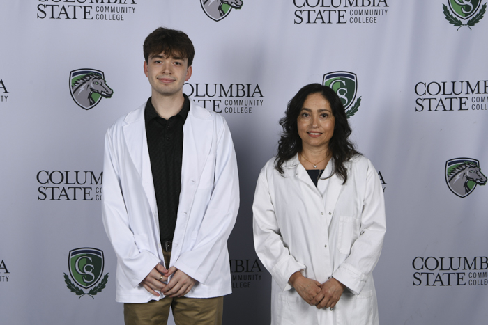 Two people stand in front of a white background.