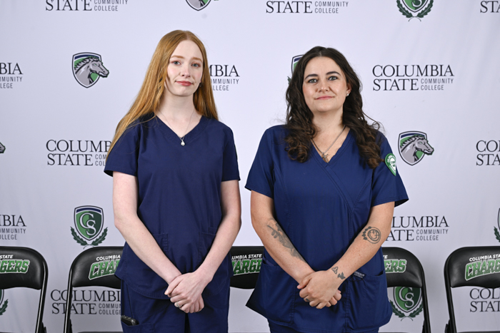 Two people stand in front of a white background.