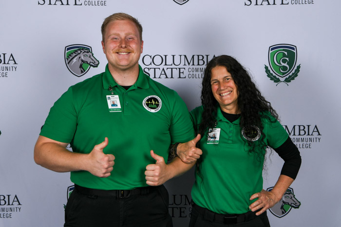 Two people pose stand in front of a white background.