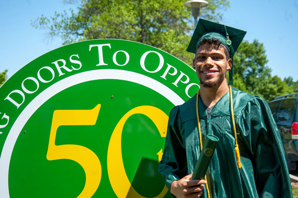 Guy in cap and gown in front of sign